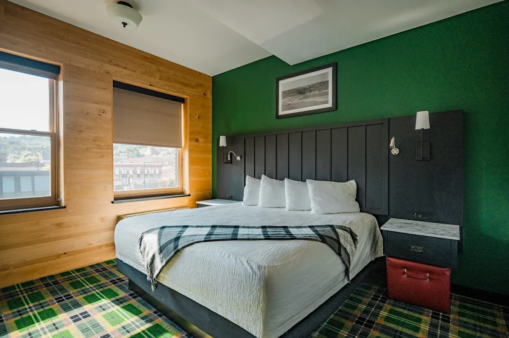 A bedroom with a green accent wall, wood-paneled walls, a bed with a plaid throw, and green plaid carpeting.